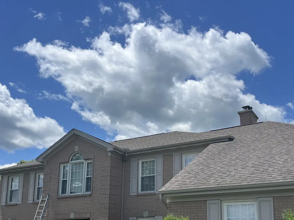 Extension ladder against a brick colonial home with a shingle roof under a blue sky