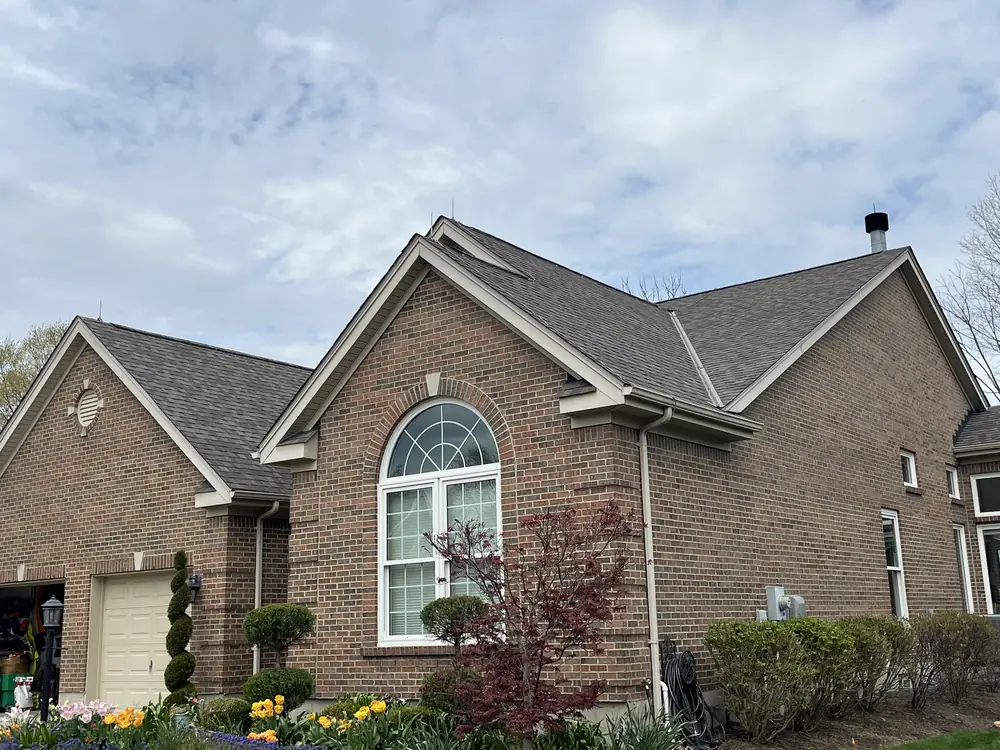 Brick home with lightning air terminals along the roof ridge and spring flowers in the beds