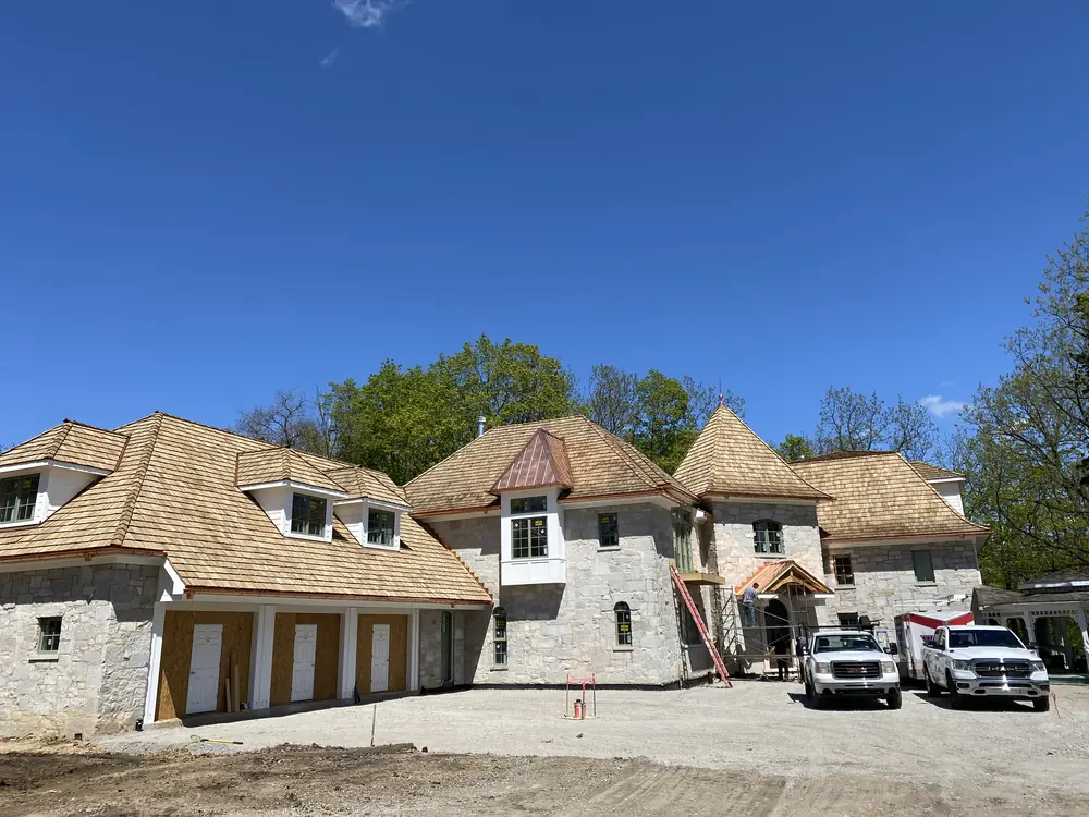 Large stone home with a new cedar shake roof during construction
