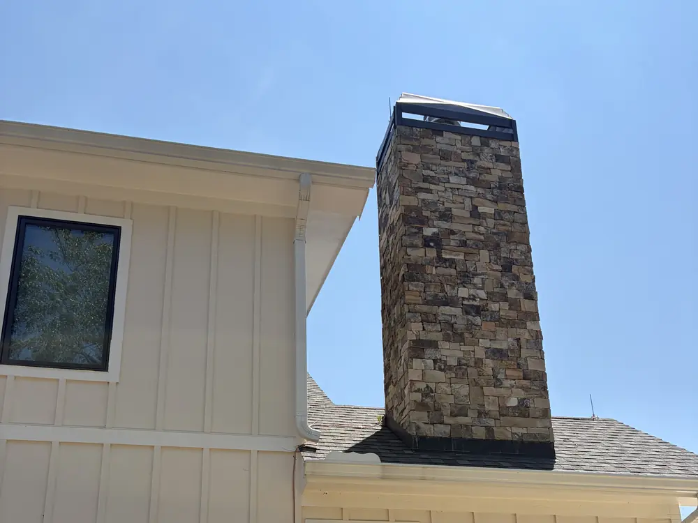 Stone chimney rising above a shingle roof on a board-and-batten home