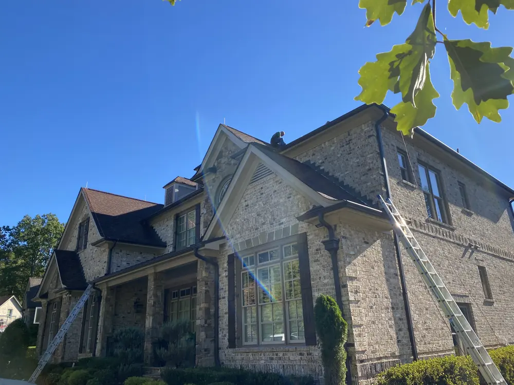 Installer on the ridge of a large brick home with ladders set at both ends of the roof