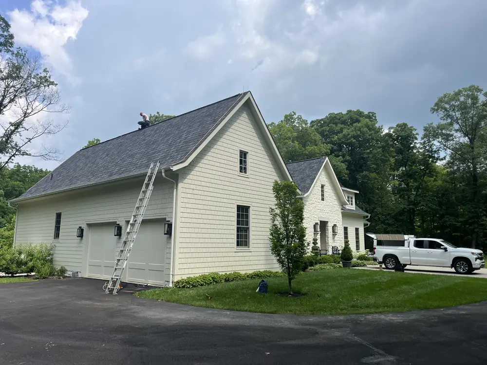 Extension ladder against a cream farmhouse with an installer working on the roof