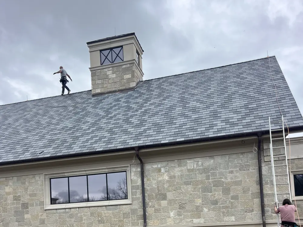 Installer walking the ridge of a slate roof beside a stone cupola