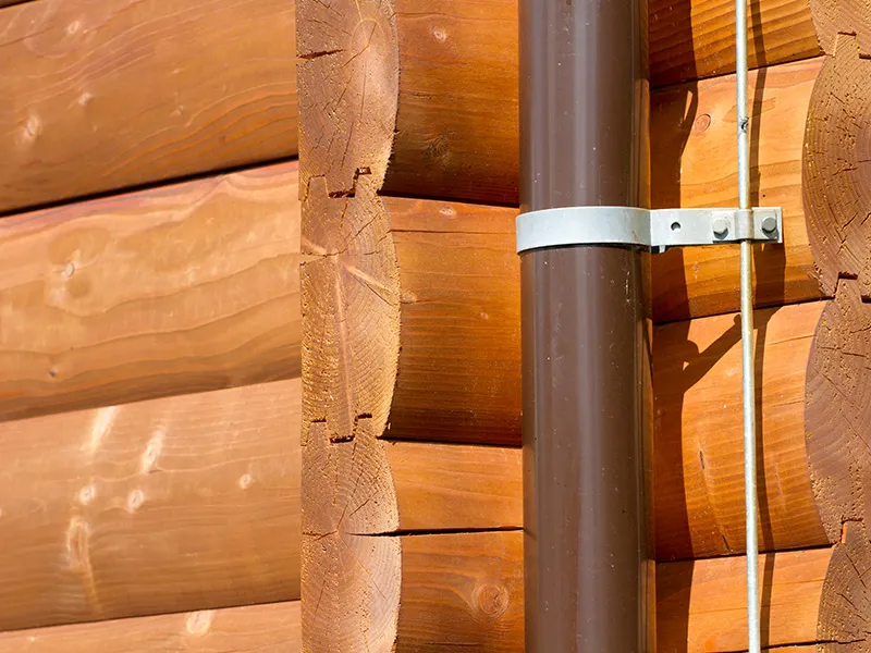 Lightning conductor cable clamped beside a downspout on a log home exterior