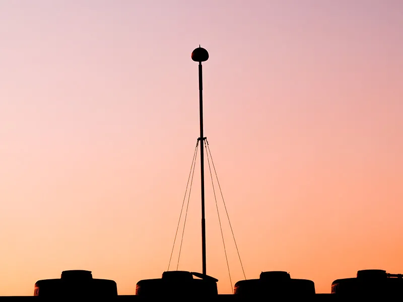 Lightning protection mast silhouetted above a rooftop at dusk